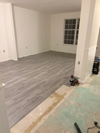 A basement mid-renovation with new gray plank flooring partially installed and tools left on the exposed subfloor.