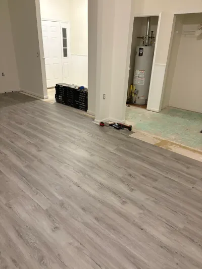 Basement mid-renovation with new gray vinyl plank flooring partially installed near a utility closet and water heater.