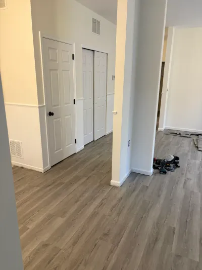 Hallway mid-renovation with new gray plank flooring, white paneled doors, and tools left on the floor.