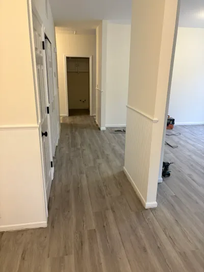 Hallway with new gray wood-look flooring and wainscoting, tools left on the floor during a renovation.
