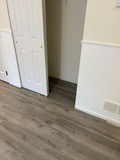 Finished room with gray vinyl plank flooring, white beadboard wainscoting, and an open closet door.