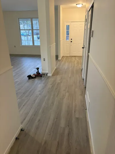 An unfurnished hallway and living area mid-renovation with new gray plank flooring and tools left on the floor.
