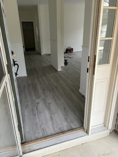 An open front door reveals a newly floored living space mid-renovation with tools left on the ground.