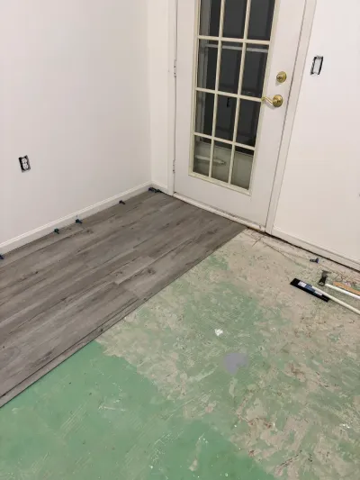 Gray plank flooring being installed over exposed subfloor near a glass-paned exterior door.