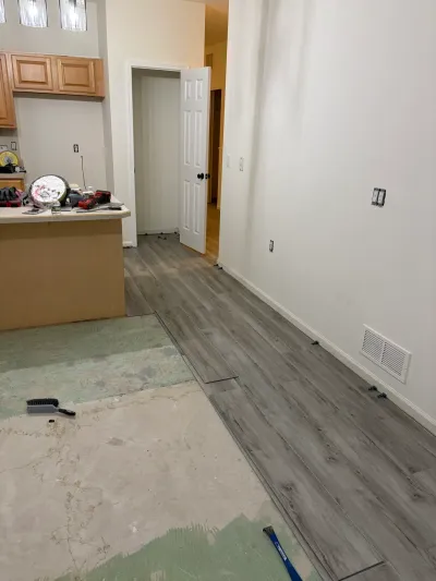 Kitchen mid-renovation with new gray plank flooring being installed over exposed subfloor.