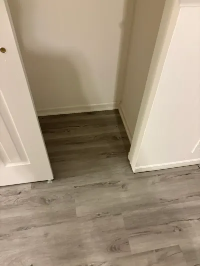 A small closet with new gray wood-look vinyl plank flooring and white walls, viewed through an open door.