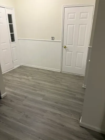 Freshly finished entryway with gray plank flooring, white beadboard wainscoting, and a white paneled door.