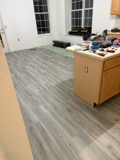 A kitchen mid-renovation with new gray plank flooring partially installed around a wooden island.
