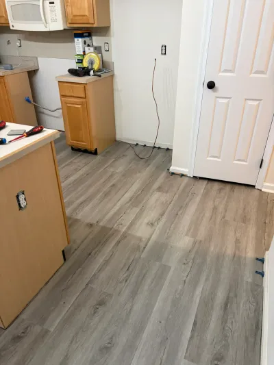 Kitchen mid-renovation with new gray plank flooring being installed around original oak cabinets.
