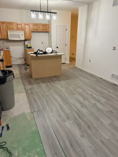 A kitchen mid-renovation with gray plank flooring being installed over green underlayment paper.