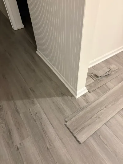Gray vinyl plank flooring being installed in a hallway with loose planks nearby.