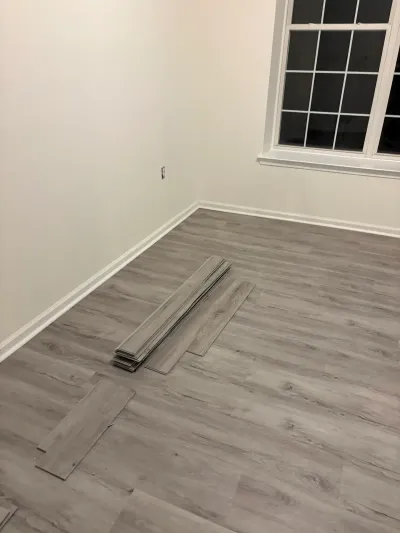 A room with gray plank flooring partially installed, with loose planks stacked on the subfloor.