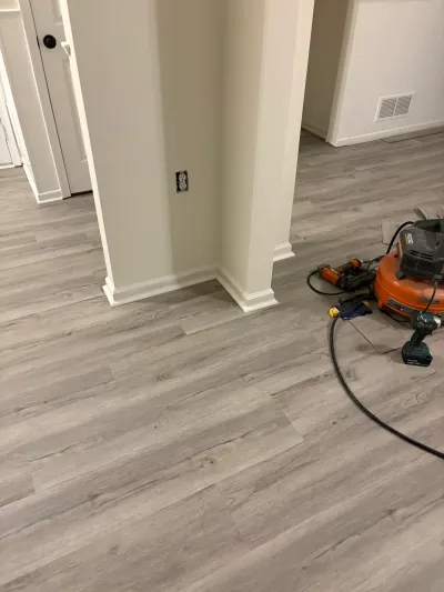 Basement flooring installation in progress with gray plank flooring and pneumatic tools on the floor.