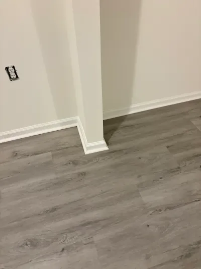 Close-up of new gray wood-look vinyl plank flooring and white baseboard trim around a wall corner.