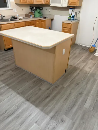 Kitchen mid-renovation with new gray plank flooring, wood cabinets, and an unfinished island.