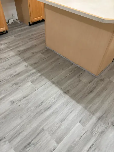 New gray plank flooring being installed in a kitchen with unfinished wood cabinets.