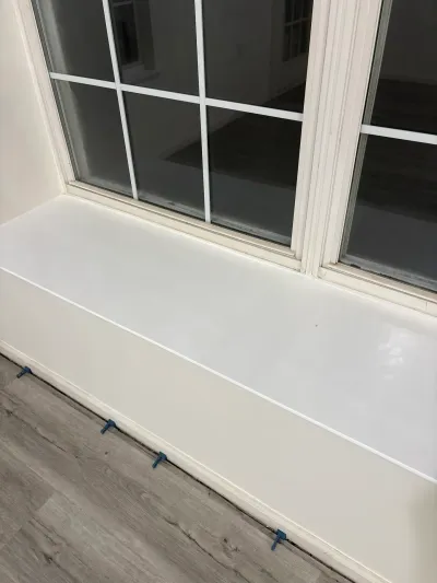 Close-up of a freshly painted window sill above new gray wood-look plank flooring with spacers still in place.