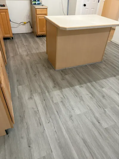Kitchen mid-renovation with new gray plank flooring, oak cabinets, and an island awaiting final touches.
