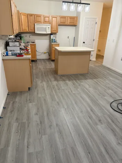 Kitchen mid-renovation with new gray plank flooring, oak cabinets, and an unfinished island base.