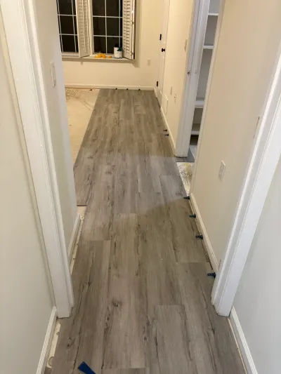 A hallway with new gray plank flooring partially installed, leading to a room with exposed subfloor.