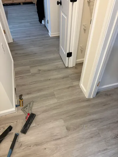 A hallway mid-installation of gray wood-look vinyl plank flooring, with tools scattered on the floor.