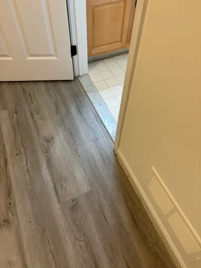 Hallway with gray plank flooring transitioning through a doorway to a tiled room with wood cabinets.