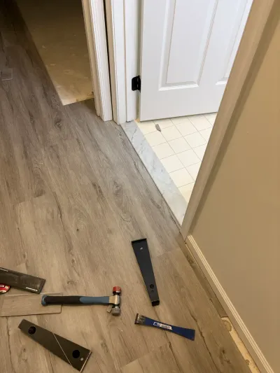 Hallway mid-installation of vinyl plank flooring with tools on the floor and a bathroom visible through an open door.