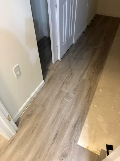 A basement hallway mid-installation, with new wood-look vinyl plank flooring laid next to bare concrete subfloor.