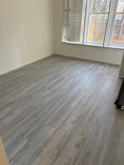 Empty room with new gray wood-look vinyl plank flooring and a bay window with white shutters.