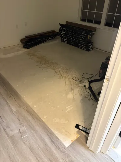 A room with bare concrete subfloor and stacked flooring boxes, next to a room with new plank flooring.
