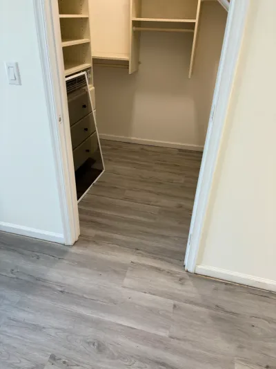 Two walk-in closets with built-in shelving, hanging rods, and new gray plank flooring.