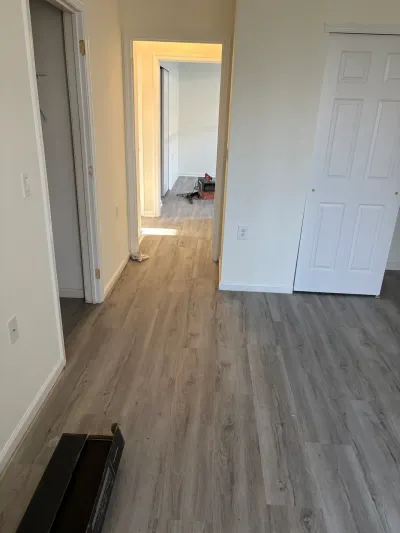 A hallway with newly installed gray wood-look vinyl plank flooring and an open door revealing another room in progress.