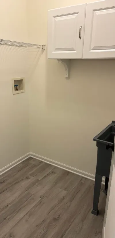 Finished laundry room with white cabinet, wire shelving, utility sink, and gray plank flooring.