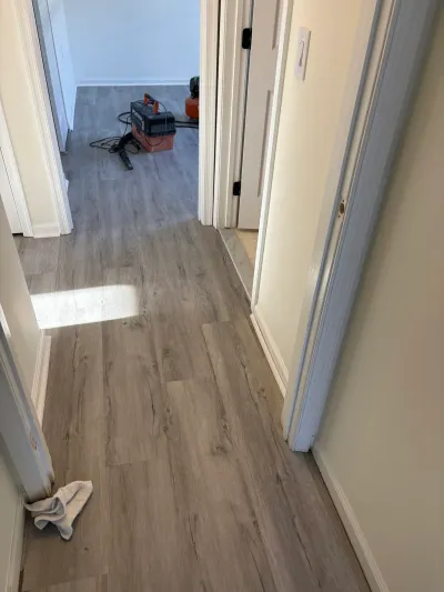 Hallway with newly installed gray vinyl plank flooring and tools visible in an adjoining room during renovation.