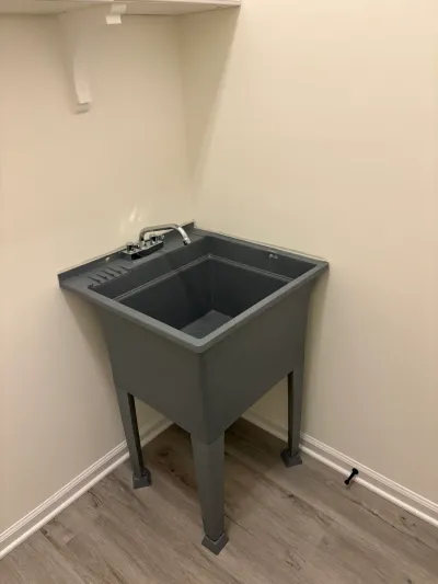 A gray freestanding utility sink with a chrome faucet sits in the corner of a laundry room.