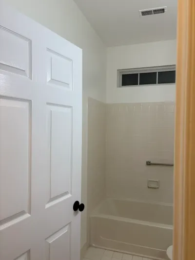 View into a dated bathroom with a beige tiled tub surround and a white paneled door.