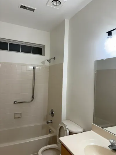 Dated bathroom with beige tile tub surround, grab bar, and adjacent toilet and vanity.