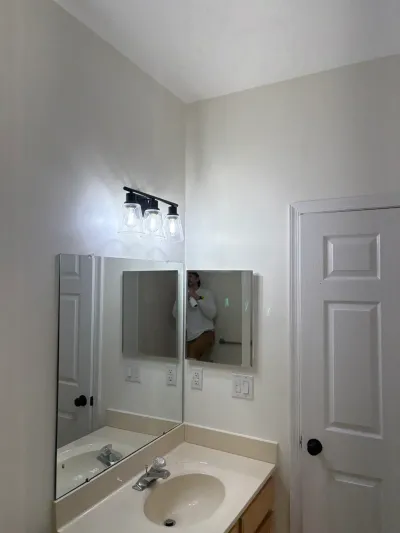 Bathroom vanity with oval sink, chrome faucet, and a black three-light fixture above the mirror.