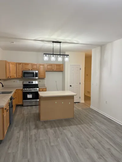 Kitchen with light wood cabinets, stainless appliances, an island, and gray plank flooring.