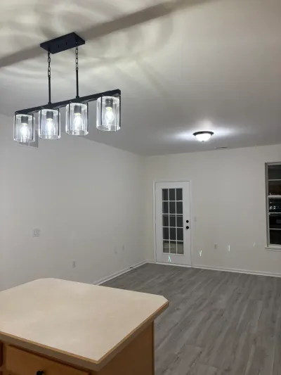 A newly finished kitchen with a black glass-shade chandelier over an island, opening into a room with gray plank flooring.