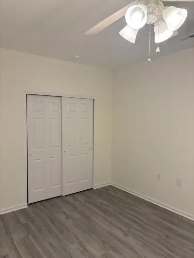 Empty bedroom with gray LVP flooring, white sliding closet doors, and a ceiling fan light fixture.