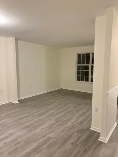 Empty finished basement room with gray vinyl plank flooring, cream walls, and a paned window.