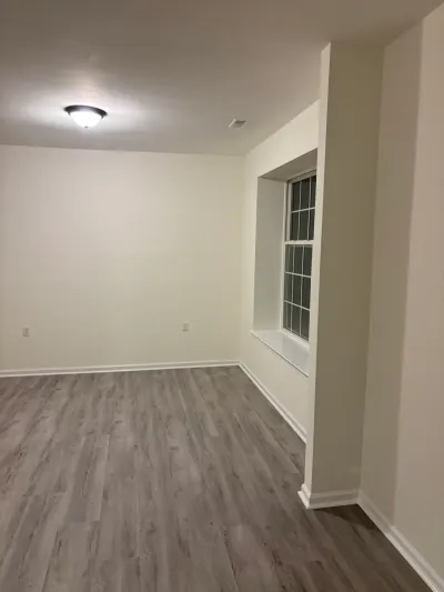 Empty finished basement room with gray vinyl plank flooring, white walls, and a recessed window.