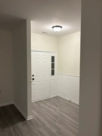 A freshly finished entryway with a white paneled front door, wainscoting, and gray plank flooring.
