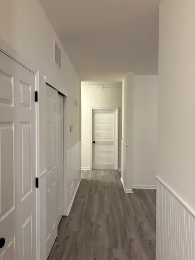 A finished hallway with gray wood-look flooring, white wainscoting, and closet doors with black hardware.
