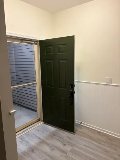 Entryway with a dark green paneled door open to a glass storm door, white wainscoting, and gray plank flooring.
