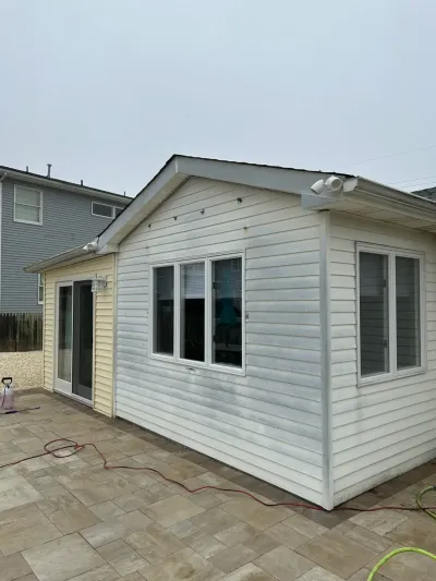 Exterior of a house addition with vinyl siding being power-washed, showing streaking and cleaning equipment on the patio.
