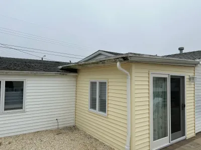 Rear corner of a house showing yellow vinyl siding addition with sliding glass door next to older white siding section.