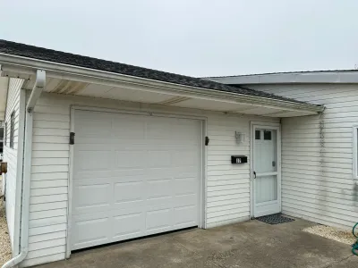 Exterior view of a home's white vinyl-sided garage and side entry door with visible siding staining under an overcast sky.