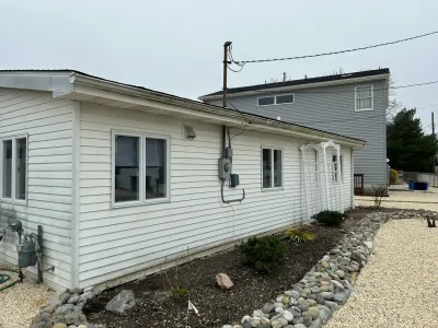 Side exterior of a white vinyl-sided home addition with a gravel path and stone-edged garden bed.